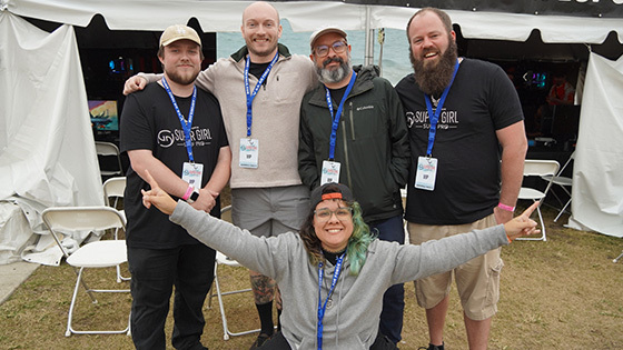 A group of five people standing in front of a large festival tent with rows of gaming computers set up inside.