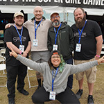 A group of five people standing in front of a large festival tent with rows of gaming computers set up inside.